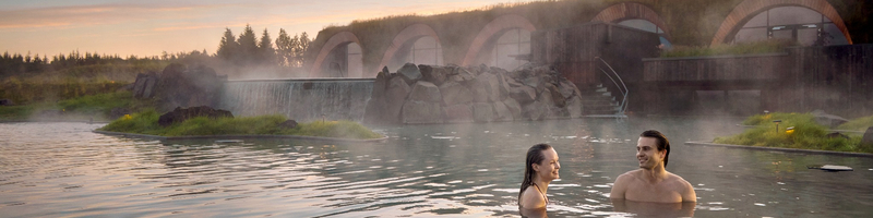 Two people bathing at Laugarás Lagoon with steam rising from the water.