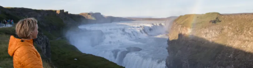 A person in an orange jacket looking out over Gullfoss waterfall.