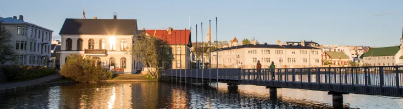 Buildings and a footbridge beside Tjörnin in Reykjavík in the evening light.