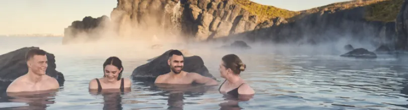 Four people bathing at Sky Lagoon among rocks and rising steam.Four people bathing at Sky Lagoon among rocks and rising steam.