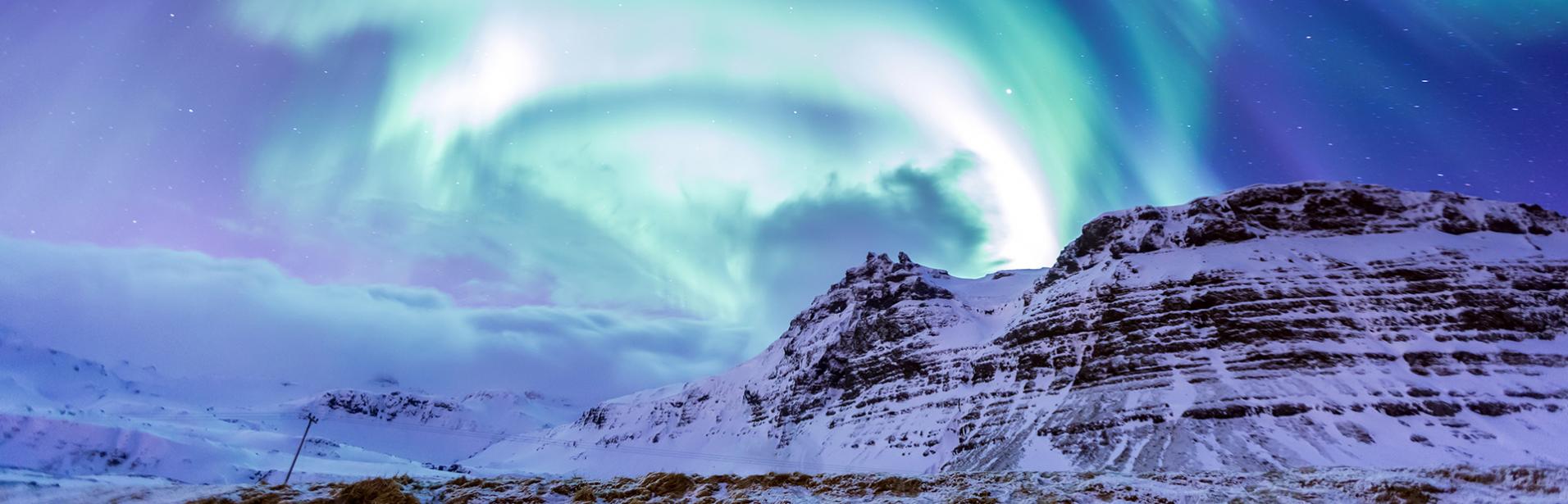 Iceland holidays northern lights tour package: northern lights in a snowy mountain terrain.