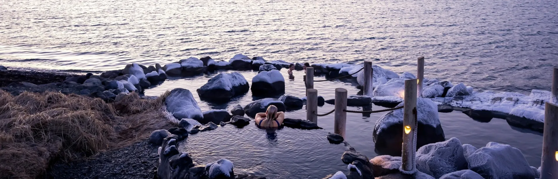 Guests bathing at Hvammsvík Hot Springs by the sea in winter.
