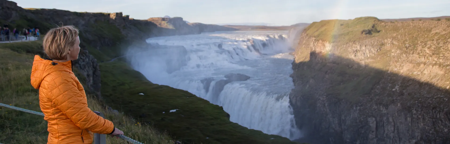 A person in an orange jacket looking out over Gullfoss waterfall.