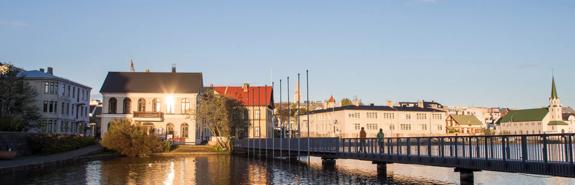 Buildings and a footbridge beside Tjörnin in Reykjavík in the evening light.