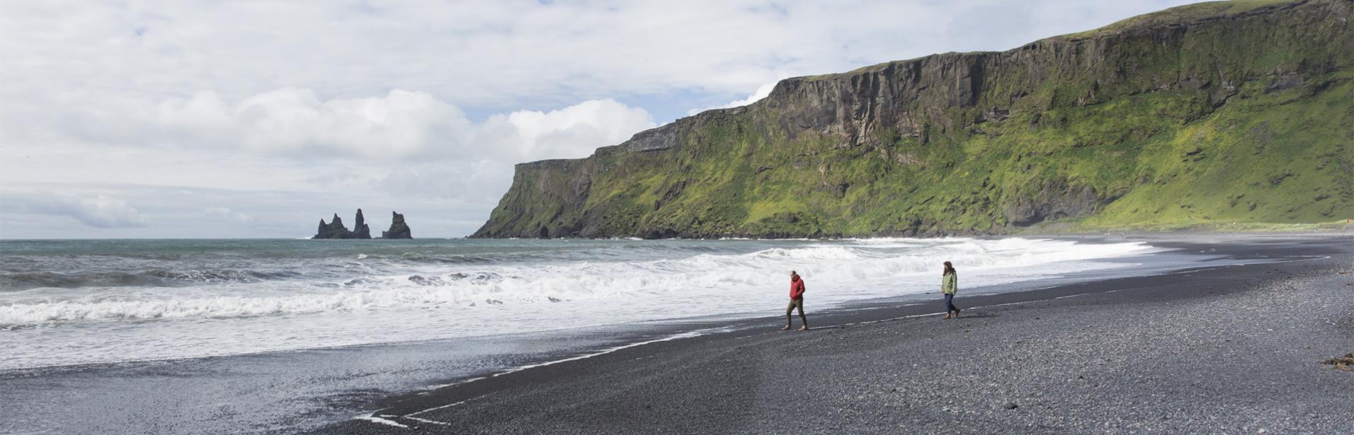 Escorted tour of Reykjavik and south coast of Iceland: couple strolling on the black beach Reynisfjara, south of Iceland.