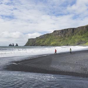Escorted tour of Reykjavik and south coast of Iceland: couple strolling on the black beach Reynisfjara, south of Iceland.
